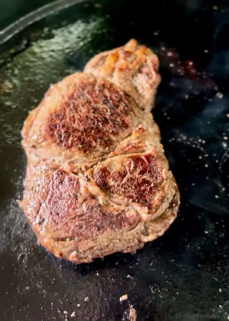 A ribeye steak with some nice browning on the outside on a cast iron pan