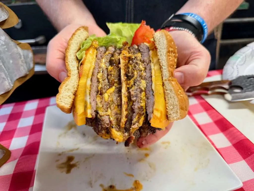 A triple decker ground pork smash burger cut down the middle The burger is displayed of a cross section both halves glistening with juices and gooey cheese