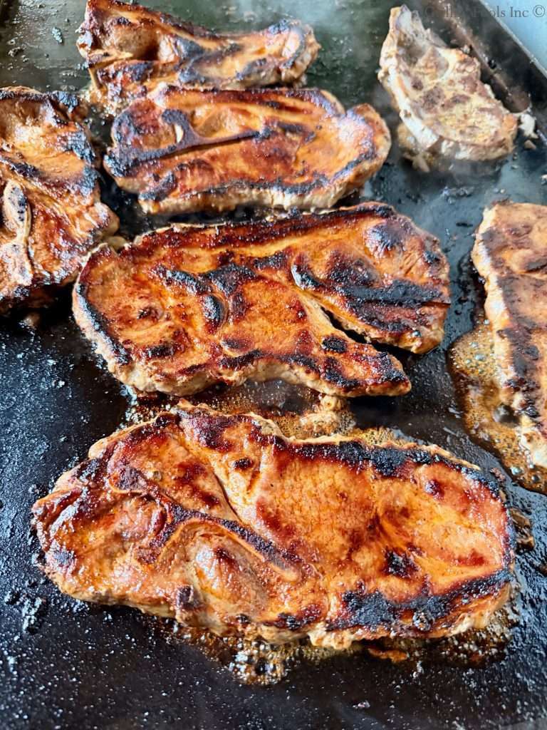 Pork Shoulder Steaks 22 | GrillinFools Several browned caramelized pork steaks cooking on a hot skillet showing crispy edges and juices simmering in the pan
