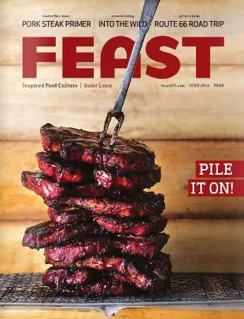 The cover of Feast Magazine featuring a stack of pork steaks with a meat fork sticking out of the top against a wooden plank back drop