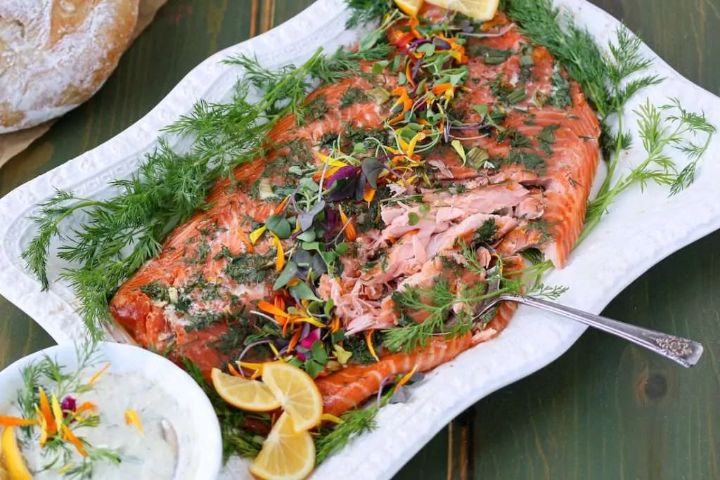 Lemon and Dill Smoked salmon on a platter next to a bowl of creamy dill sauce garnished with fresh dill and lemon slices