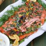 Lemon and Dill Smoked salmon on a platter, next to a bowl of creamy dill sauce, garnished with fresh dill and lemon slices