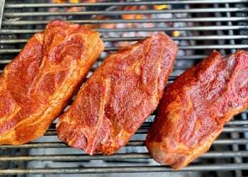 Three raw seasoned pork steaks resting on top of grill grates as viewed from directly above