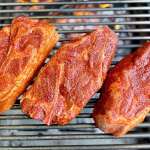 Three raw, seasoned pork steaks resting on top of grill grates as viewed from directly above
