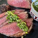 Sliced Picanha Roast with Chimichurri spooned over the top, with a bowl that reads 