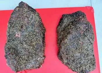 Two smoked beef briskets on a cutting board both of which have excellent blackened bark and the pic is taken from above